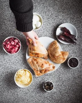 Hand holds bread, surrounded by fresh toppings and spices 库存照片