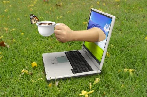 Hand holds a cup of coffee out of laptop screen Stock Photos