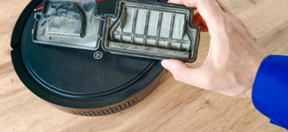 Hand holds a dirty filter while removing it from a robot vacuum cleaner on a Stock Photos