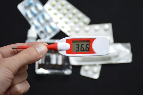 Hand holds an electronic thermometer on the background of pills Stock Photos