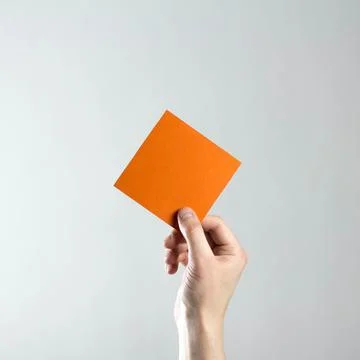 The hand holds an empty square orange sheet of paper. A clean flyer in your h Foto stock