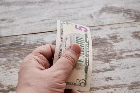 A hand holds five dollars in one bill over a worn table close-up, make a dona Foto stock