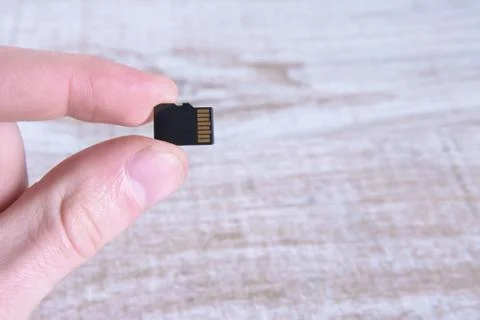 Hand holds flash drive, memory card adapter on wooden background. close up Stock Photos
