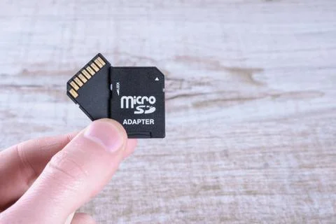 Hand holds flash drive, memory card adapter on wooden background. close up Stock Photos