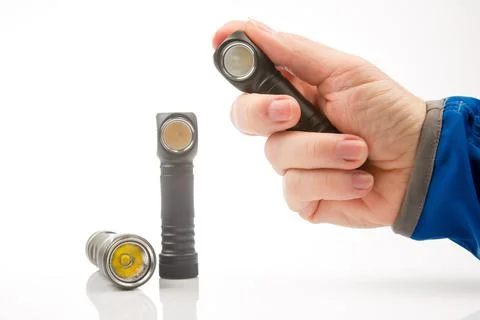 Hand holds a flashlight against the background of other flashlights on a whit Stock Photos