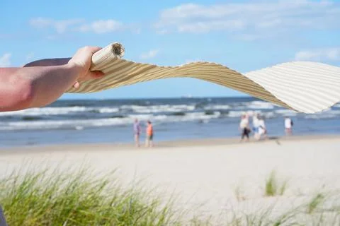 Hand holds a folded beach mat with beige stripes against the backdrop of th.. Stock Photos