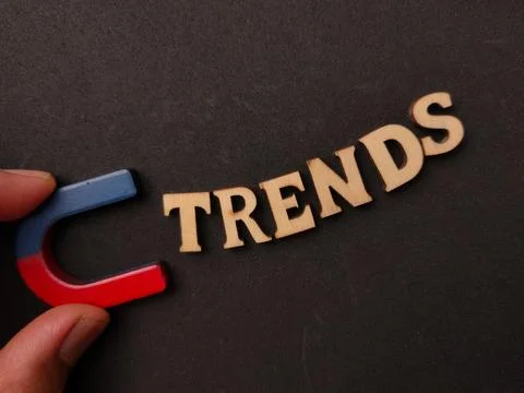 A hand holds a horseshoe magnet pulling wooden letters that spell TRENDS on.. Stock Photos