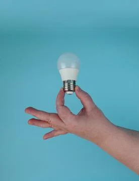 The hand holds an LED lamp with an E27 socket on a blue background. Foto stock