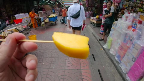 Hand holds mango slice on stick in busy Bangkok street Stock Footage 310254621