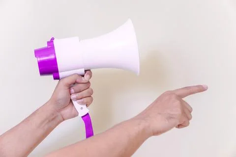 A hand holds a megaphone while pointing, indicating communication or a call.. Foto stock