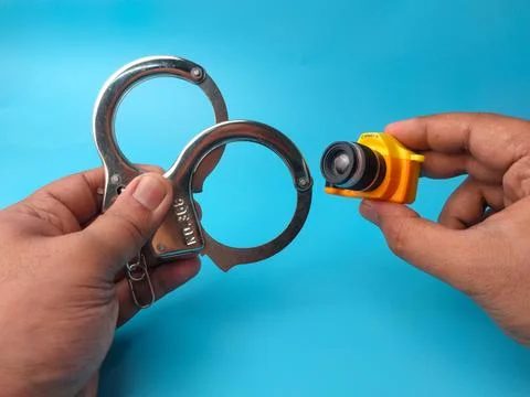 A hand holds metal handcuffs while another hand holds a tiny yellow and bla.. Stock Photos