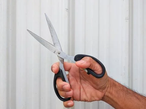 A hand holds a pair of scissors with a shiny, silver steel blade Stock Photos