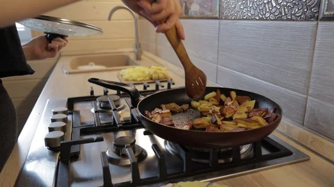 The hand holds pan lid, stirs the fried potatoes with a wooden spatula on a gas 動画素材 129246775