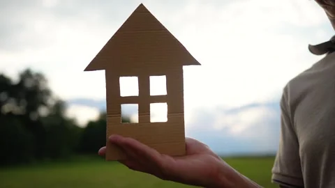 Hand holds paper house model outdoors at sunset. Person shows cardboard home Stock Footage 345958489