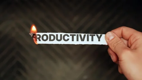 Hand holds a paper strip reading “PRODUCTIVITY” while the edge burns in flame Stock Footage 330863134