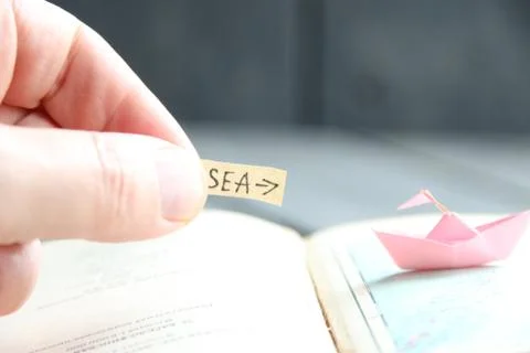 The hand holds a pointer to the sea and paper boats on the map. Stock Photos