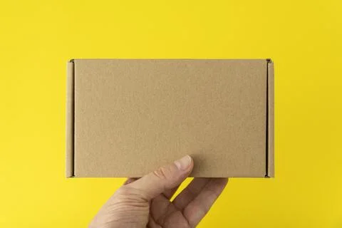 Hand holds rectangular cardboard box, yellow background. Copy space. Mock up. Stock Photos