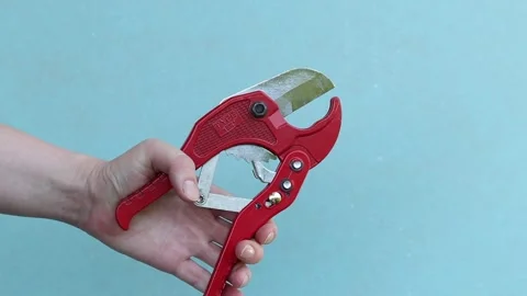 Hand holds red pipe cutter for plastic pipes on blue background Stock Footage 338003429