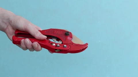 Hand holds red pipe cutter for plastic pipes on blue background Stock-Footage 338003433