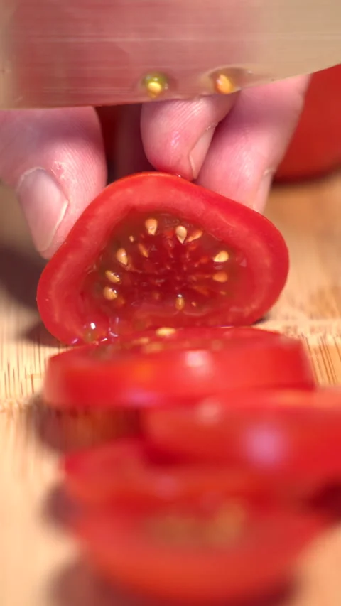 A hand holds a red tomato on a cutting board and slices it with a knife Stock Footage 341345850