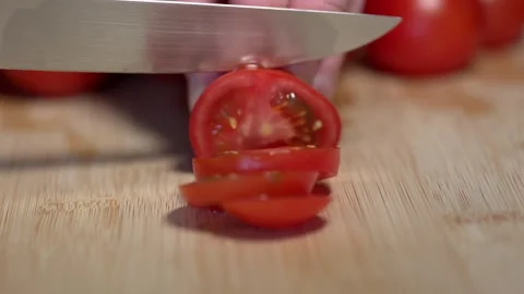 A hand holds a red tomato on a cutting board and slices it with a knife Stock Footage 341345885
