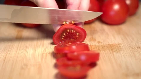 A hand holds a red tomato on a cutting board and slices it with a knife Stock Footage 341345911