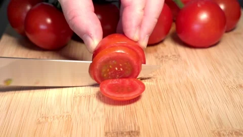 A hand holds a red tomato on a cutting board and slices it with a knife Stock Footage 341345987