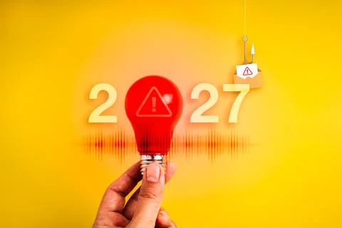 Hand holds red warning light bulb beside 2027 and hooked email envelope on .. Stock Photos