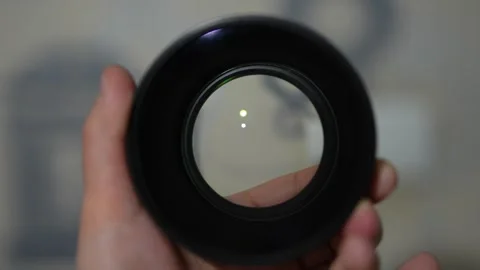 Hand holds a round camera lens, reflecting soft green and yellow light Stock Footage 330188420