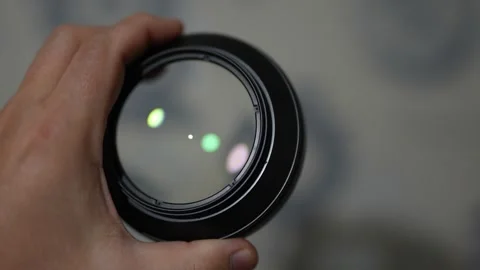 Hand holds a round camera lens, reflecting soft green and yellow light Stock Footage 330188430