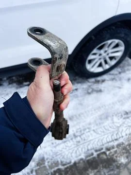 Hand holds a rusty Ford Explorer car part with snow and a nearby wheel in a.. Stock Photos