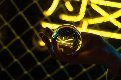 A hand holds a shining ball with a reflection of neon lights. Storyteller of  Illustrazione stock