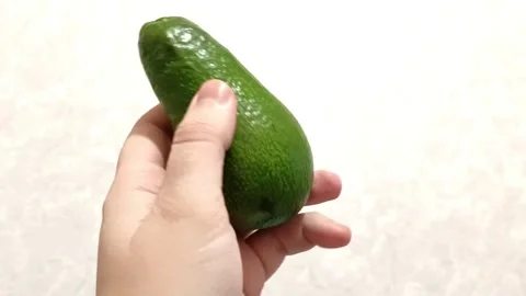 A hand holds a single, small avocado against a white background. Stock Footage 292757580