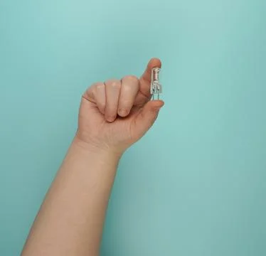The hand holds a small capsule halogen lamp on a turquoise background. Stock Photos