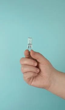 The hand holds a small capsule halogen lamp on a turquoise background. Foto stock