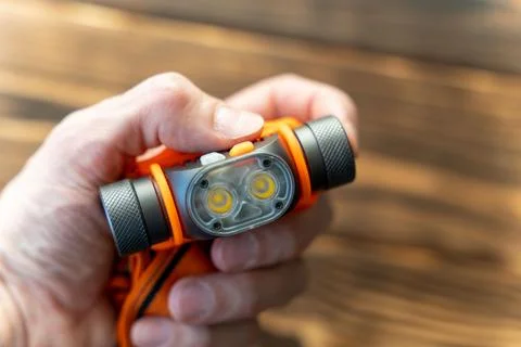 Hand holds a small flashlight with orange and silver colors on a wooden surfa Stock Photos