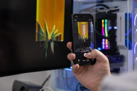 Hand holds smartphone capturing a broken computer monitor with a cracked sc.. Foto stock