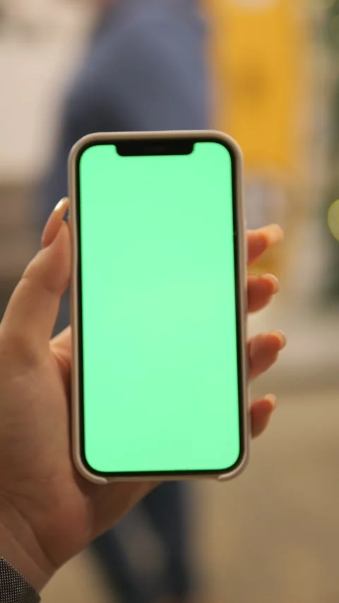 A hand holds a smartphone with a green screen for customizations and Stock Footage 296729808