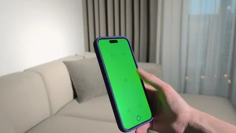Hand holds smartphone with green screen in a living room. Finger taps and s.. Stock Footage 337774117
