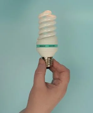 The hand holds a spiral CFL with an E27 socket on a turquoise background. Stock Photos