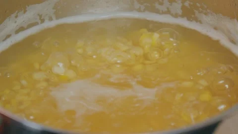 A hand holds a spoon while stirring lentils simmering in a stainless steel pot Stock Footage 308254954