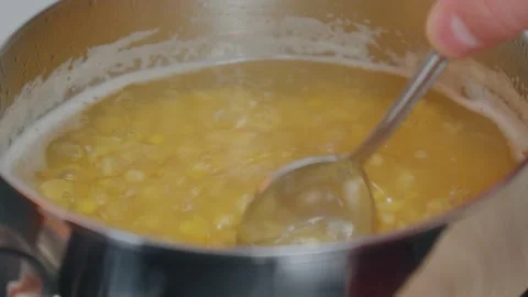 A hand holds a spoon while stirring lentils simmering in a stainless steel pot Stock Footage 309416726