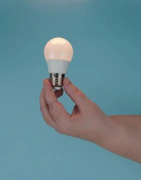 The hand holds the switched-on E27 LED lamp on a blue background. Foto stock