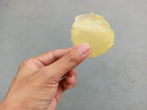 Hand holds thin, delicate, pale yellow food item Stock Photos