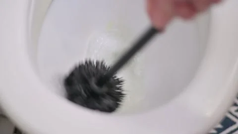 A hand holds a toilet brush while applying a cleaning solution in a toilet bowl. 库存影片 337101320