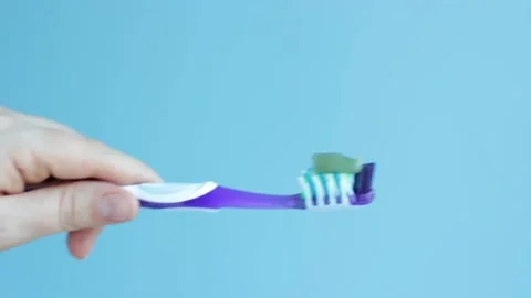Hand holds a toothbrush with green toothpaste on blue background. Stock Footage 154281868