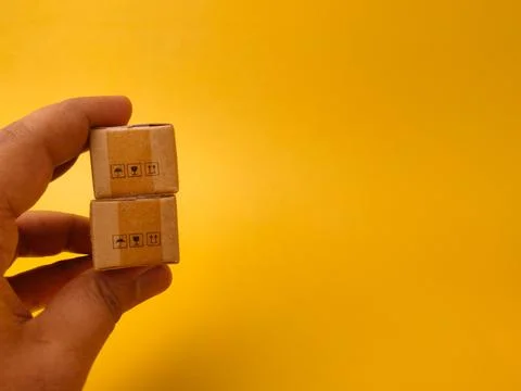 A hand holds a vertical stack of two small brown cardboard boxes against a .. Stock Photos