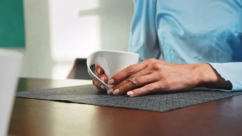 Hand holds a white mug with coffee while sitting at a table in the living room Video stock 205325119