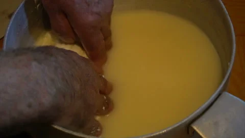Hand in hot fermented sheep's milk collects large lump of cheese in a wooden 스톡 동영상 94239591
