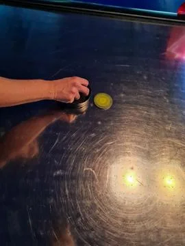 A hand hovering over a yellow puck on an air hockey table. Stock Photos